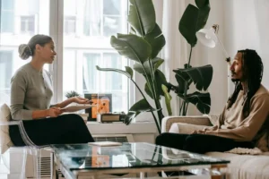 Psychologist taking notes during a therapy session while listening to a client discussing personal concerns on a sofa